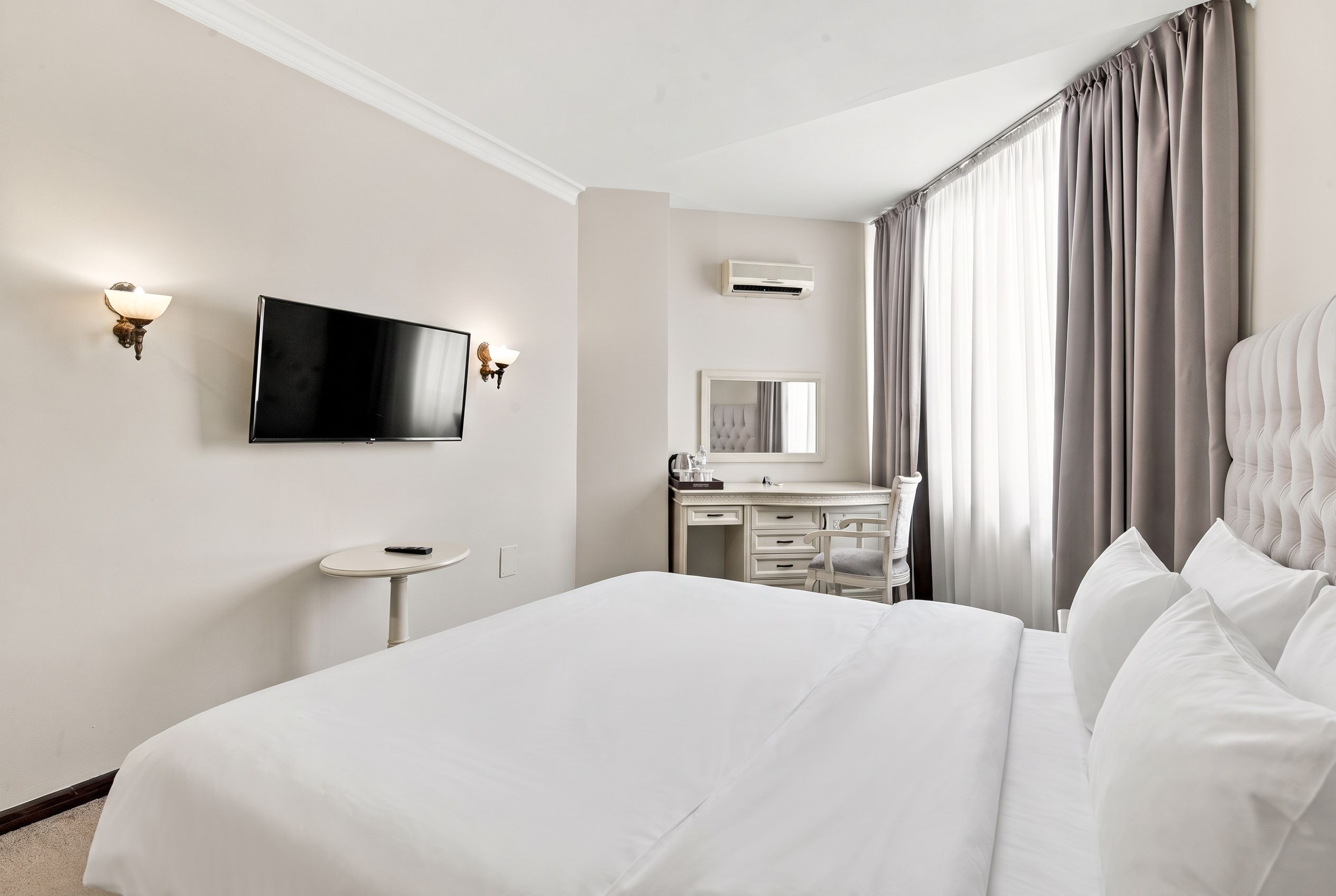A hotel room with a bed, a desk, a chair, a television, and a window with curtains.
