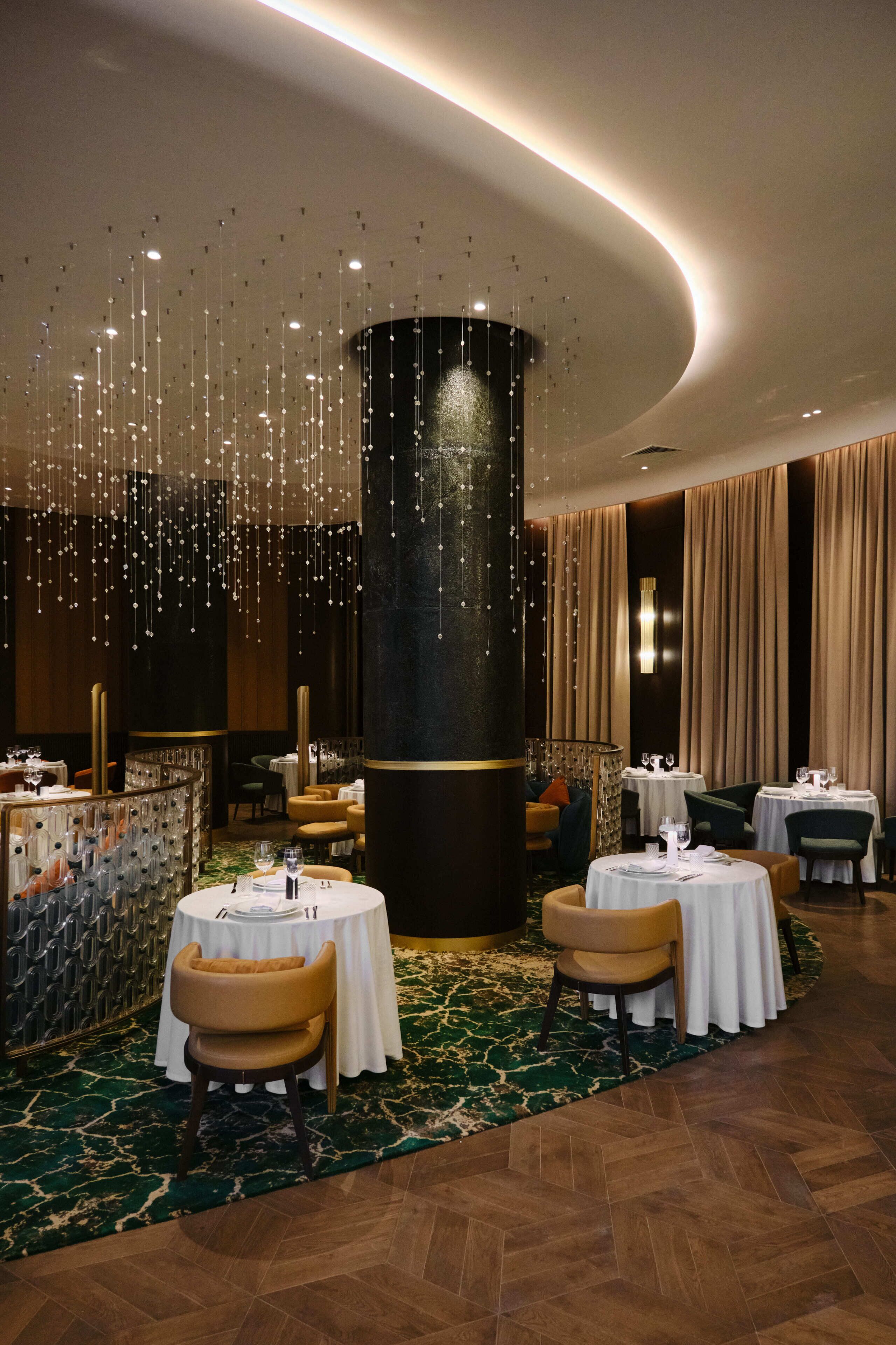 Un restaurant avec des tables rondes, des chaises, des luminaires suspendus et un tapis à motifs.