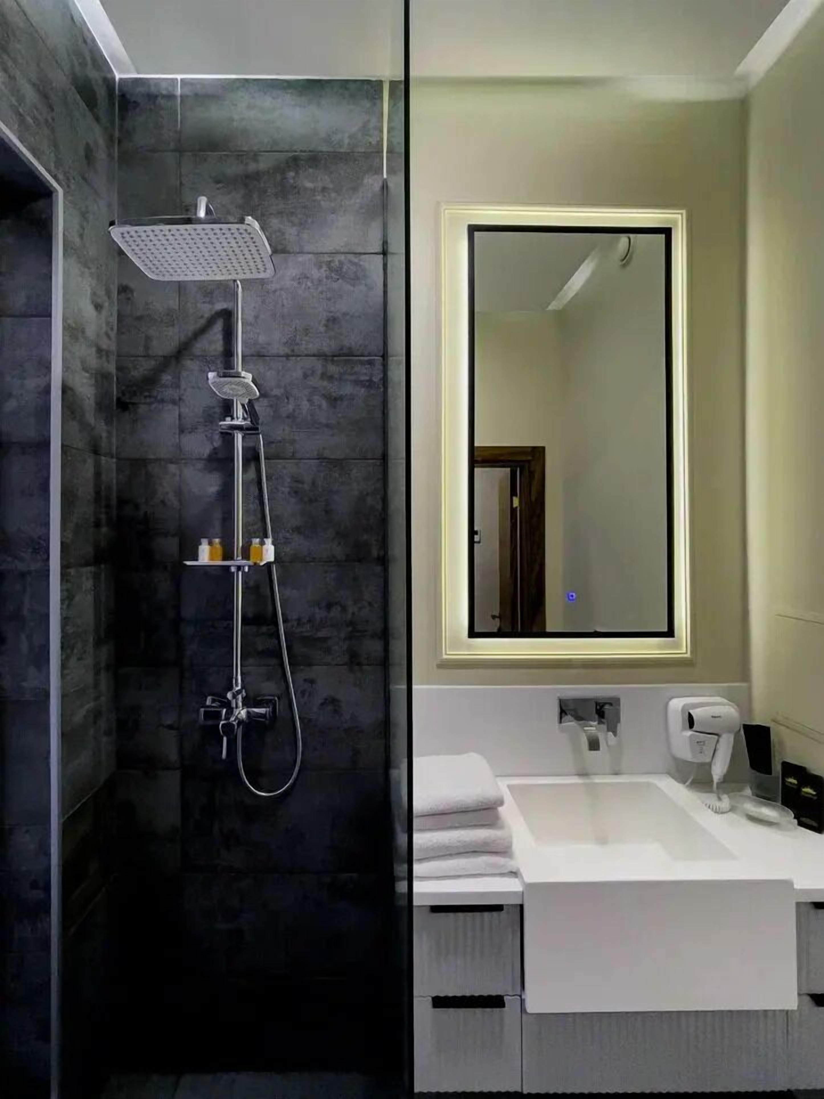 Een moderne badkamer met een douchecabine van glas, een grote spiegel en een wit wastafelmeubel met een handdoekhouder.