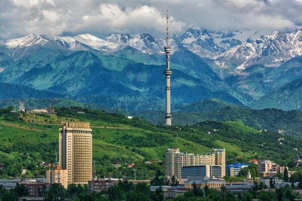 A cityscape with a prominent tower, surrounded by mountains and greenery. - Hotel Kazakhstan (Almaty)