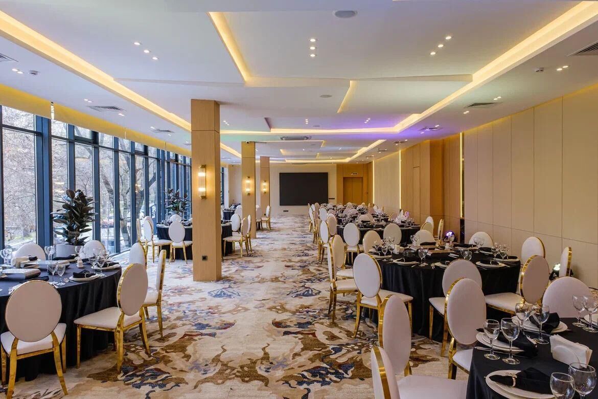 Une salle de banquet avec des tables rondes, des chaises blanches et un sol recouvert de moquette.