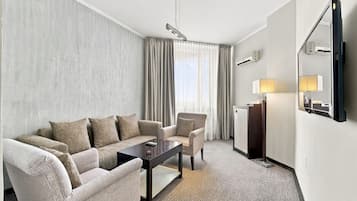 Una habitación de hotel con sofá, sillón, una mesita, televisor y lámpara.