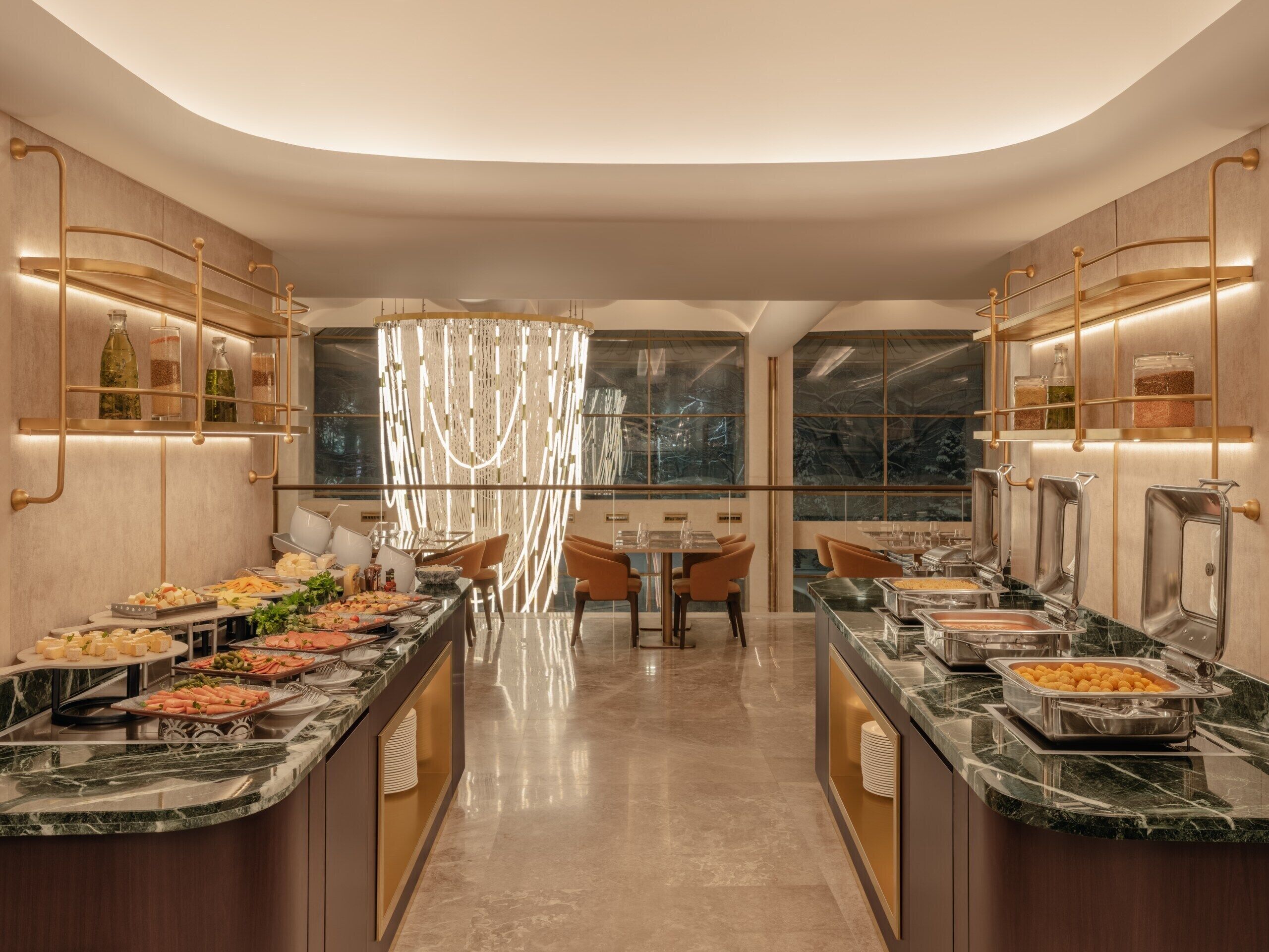 Une cuisine d’hôtel moderne, dotée de plans de travail en marbre, de buffets et d’un lustre.
