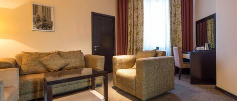 A furnished living room with a sofa, armchairs, a coffee table, a desk, and a chair.