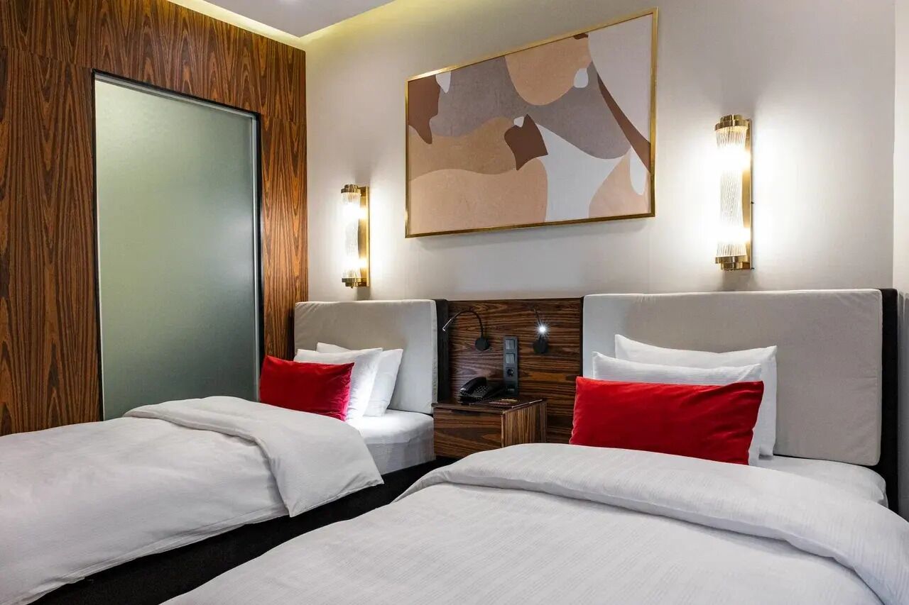 Een hotelkamer met twee bedden, een wandpaneel van hout, een modern abstract schilderij en wandlampen.