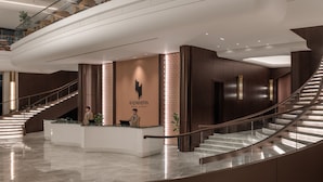 A modern hotel lobby with a curved reception desk, a staircase, and a high ceiling. - Hotel Kazakhstan (Almaty)