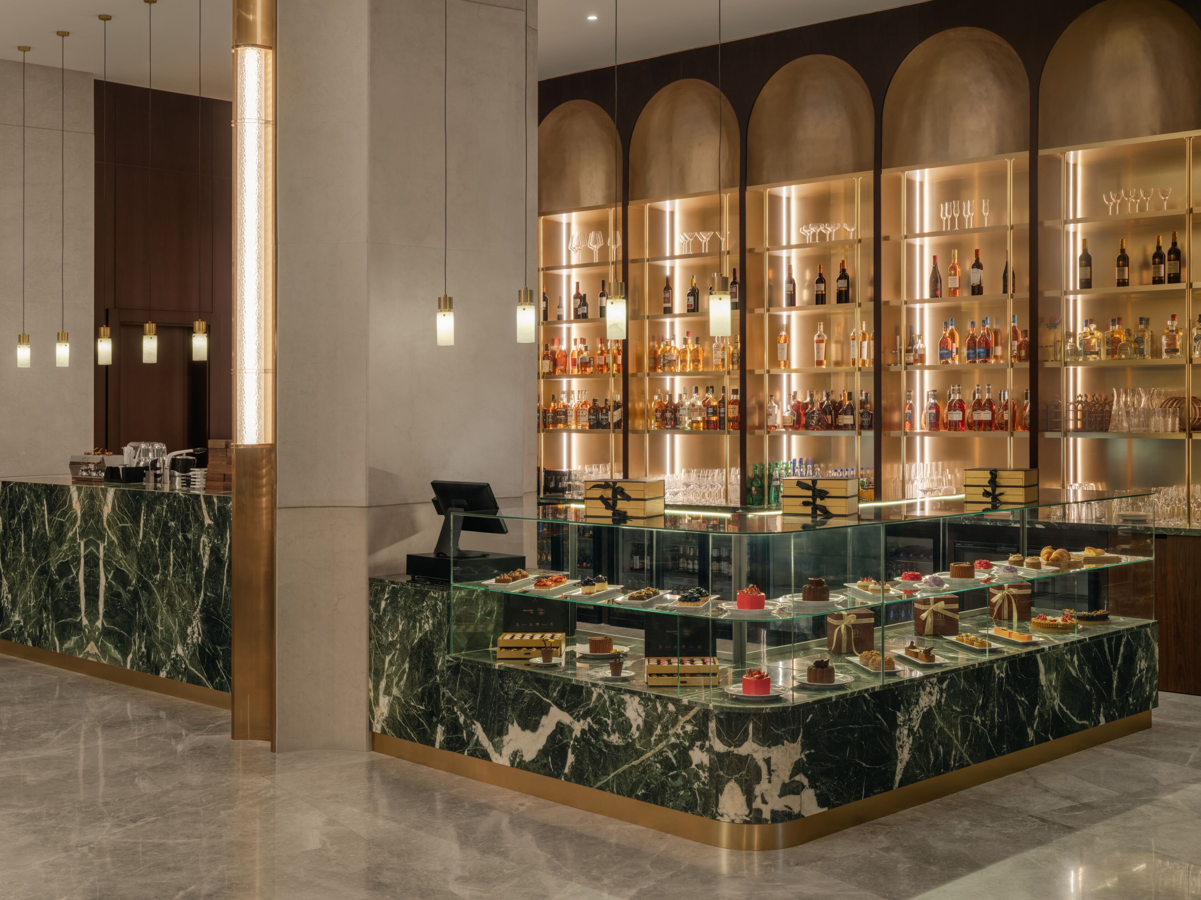 A bar area with a marble counter, shelves of liquor bottles, and a glass display case with desserts.