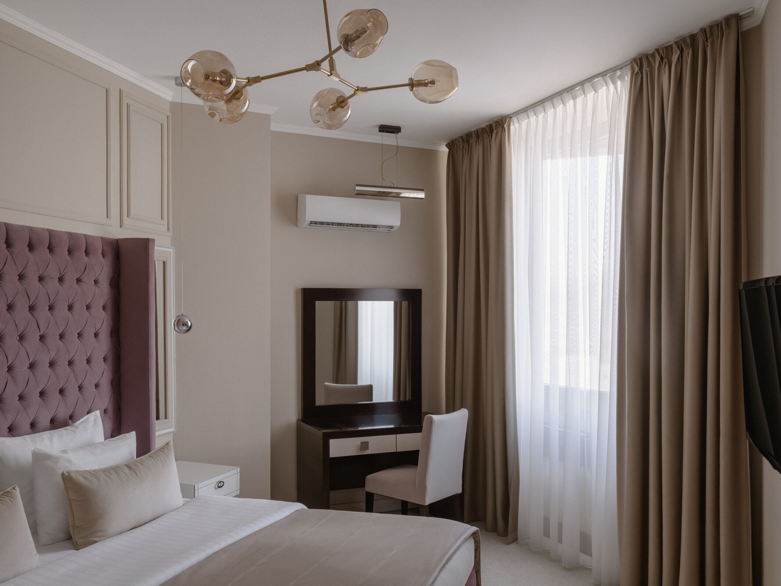 A hotel room with a tufted headboard, a large mirror, a desk, and a chair.