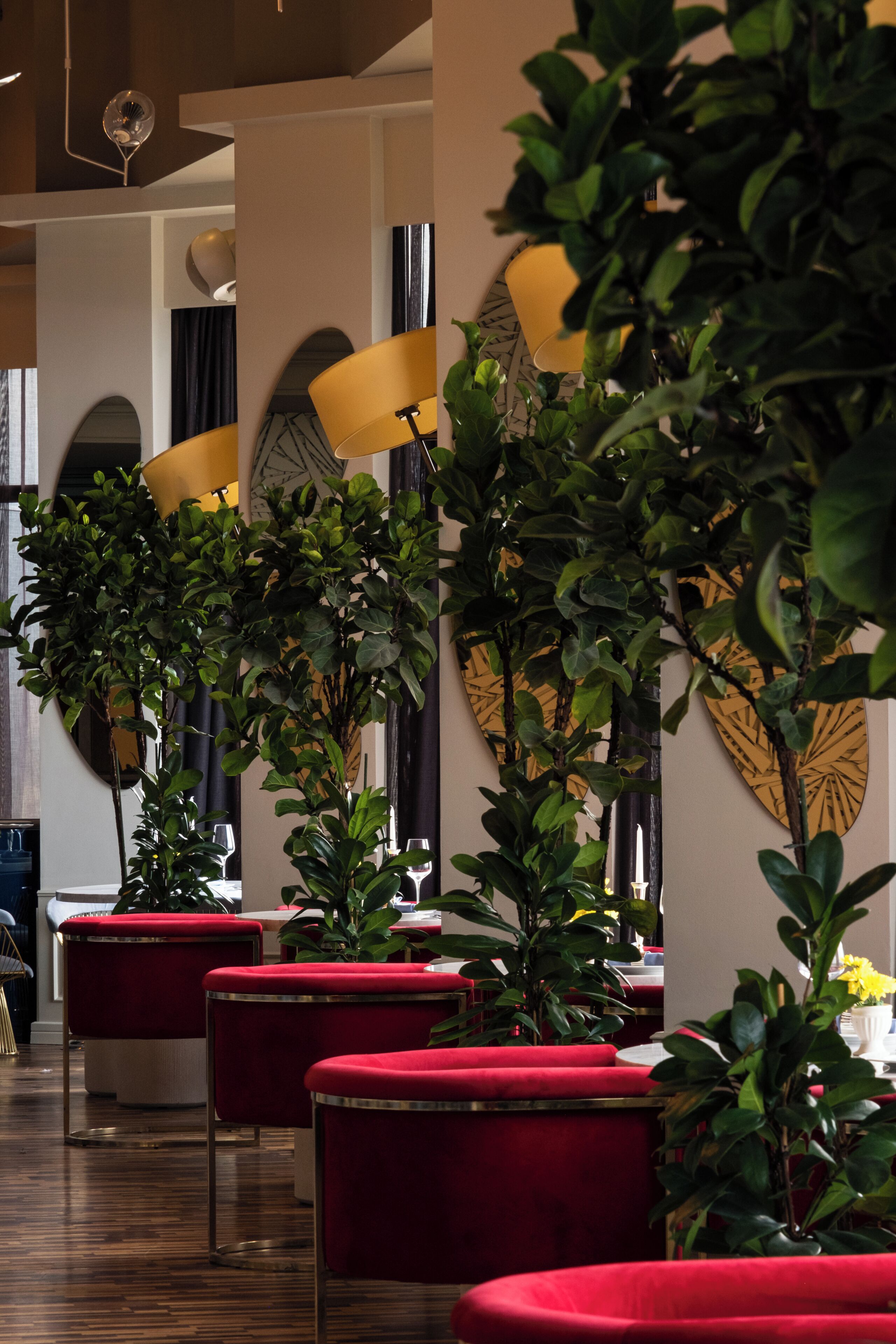 A modern interior with red upholstered seating, tall floor lamps, and green plants.