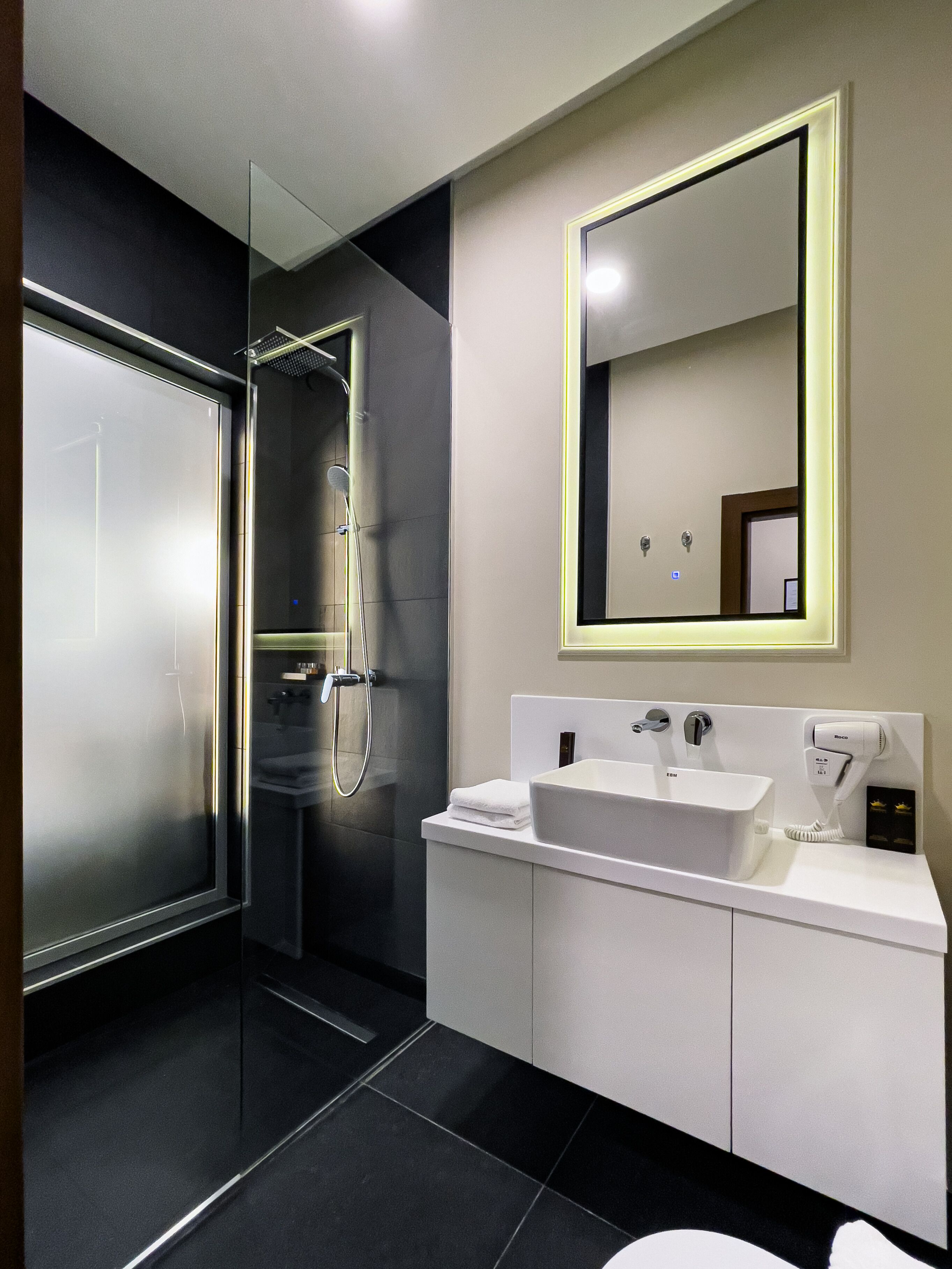 A modern bathroom with a glass shower enclosure, a large mirror, and a white vanity with a sink and towel rack.