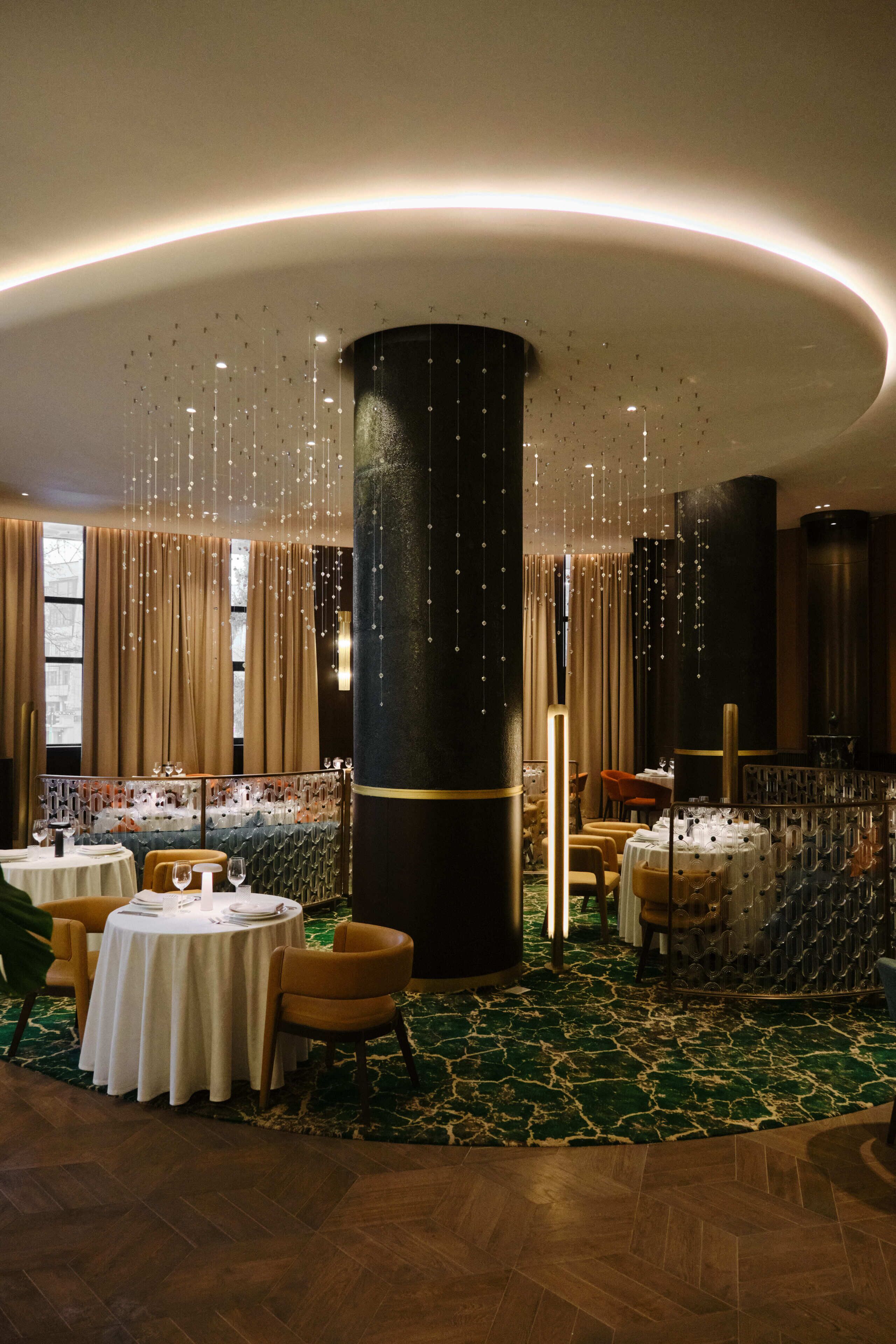Un restaurante con mesas redondas, sillas, una alfombra estampada de color verde y un pilar grande.