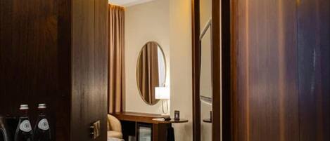 A hotel room with a bed, a desk with a lamp, a minibar, and a large mirror.