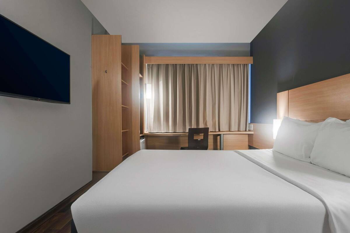 A hotel room with a bed, a desk, a chair, and a television.