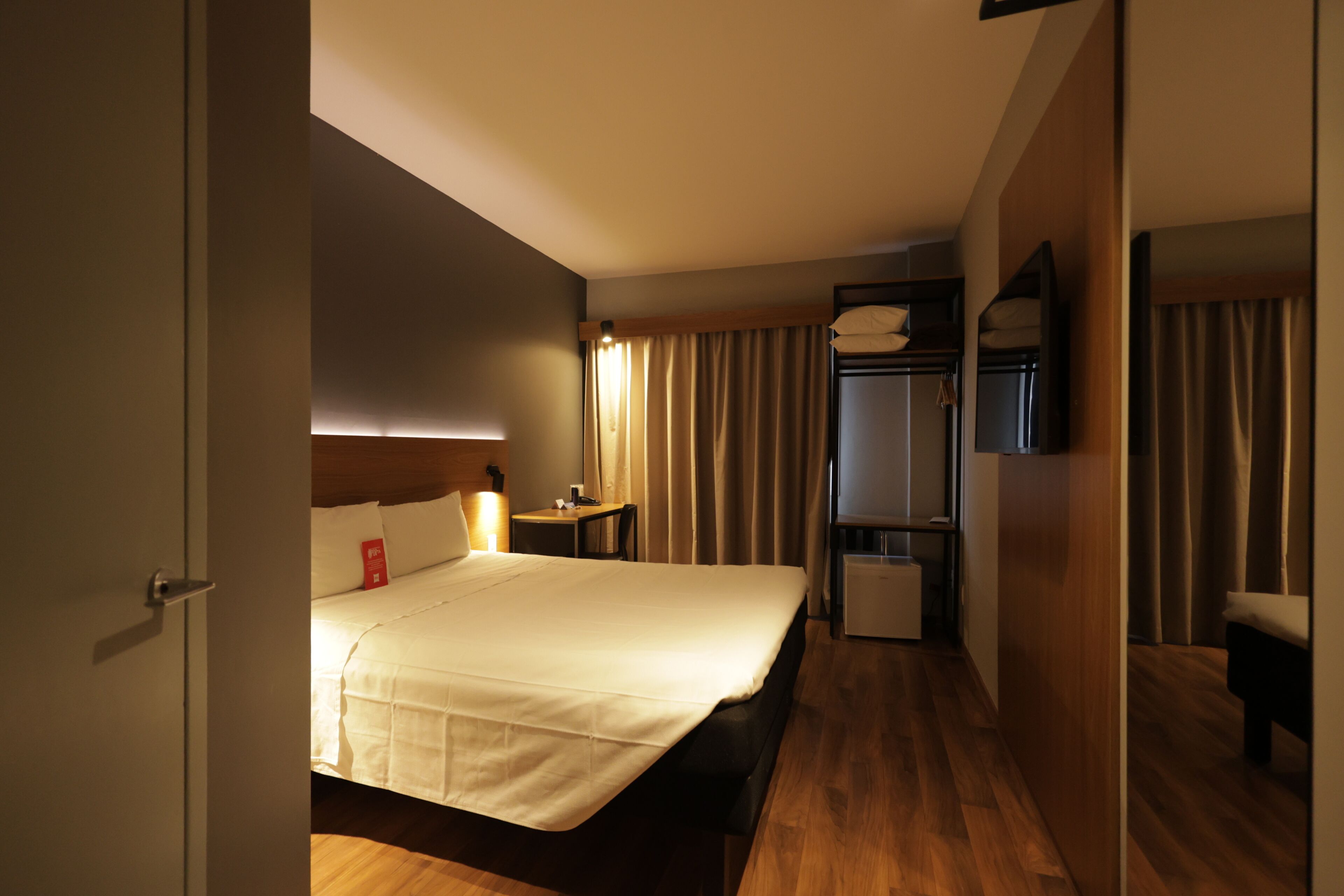 A hotel room with a bed, bedside table, lamp, and a mirror.