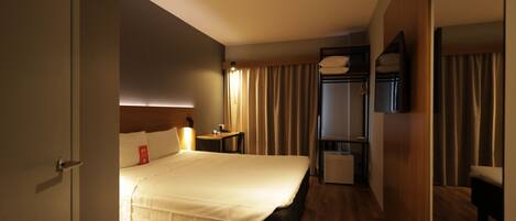 Een hotelkamer met een bed, nachtkastje, lamp en een spiegel.
