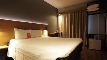 Habitación de hotel con una cama grande, mesitas de noche, un escritorio, una silla, un armario y una ventana con cortinas.