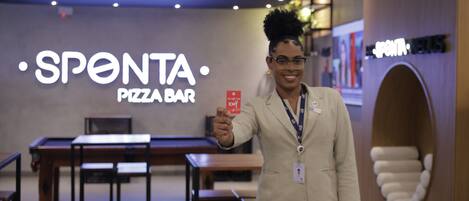 Una persona sosteniendo una tarjeta roja frente al letrero de Sponta Pizza Bar.