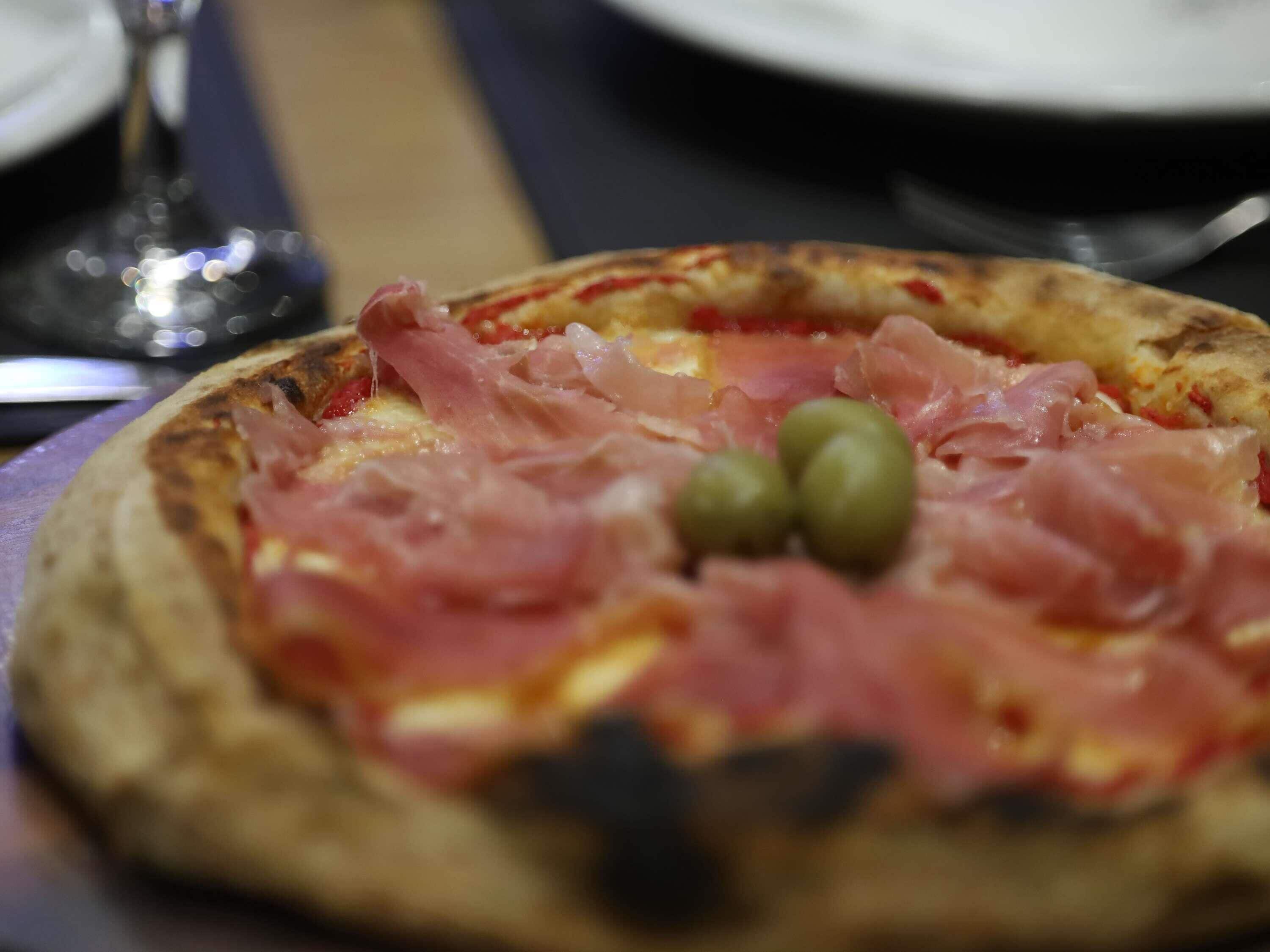 Una pizza con jamón y aceitunas sobre una mesa.