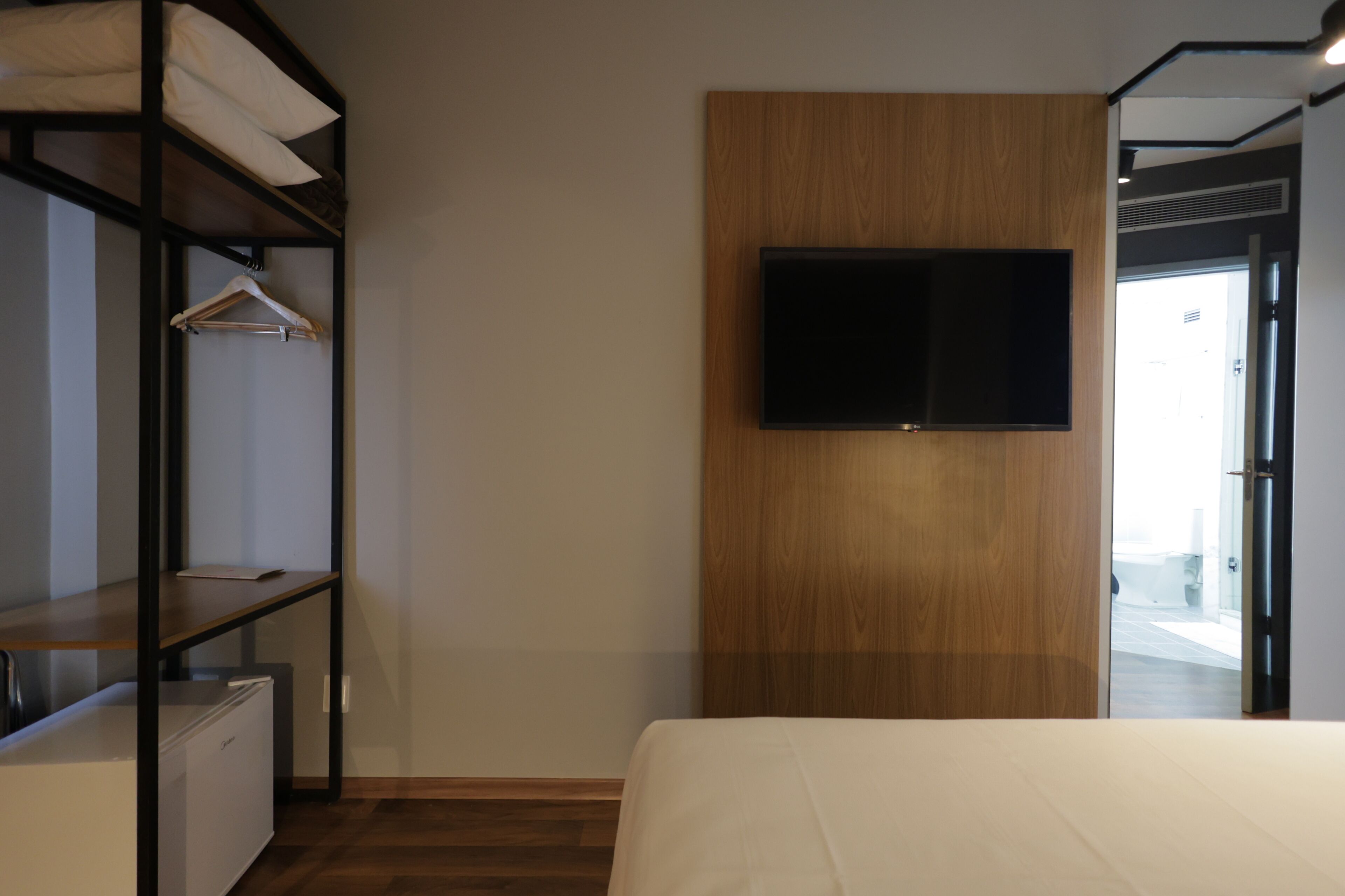 Ein Hotelzimmer mit einem Bett, einem Kleiderschrank, einem an einer Holzplatte montierten Fernseher und einem kleinen Schreibtisch mit Stuhl.