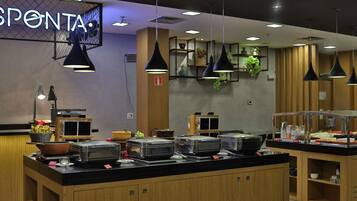 Uma área de buffet com um letreiro escrito 'SPONTA', diversas estações de comida e iluminação pendente.