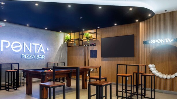 Un bar à pizzas PENTA avec une table de billard, des tabourets de bar et un grand écran.
