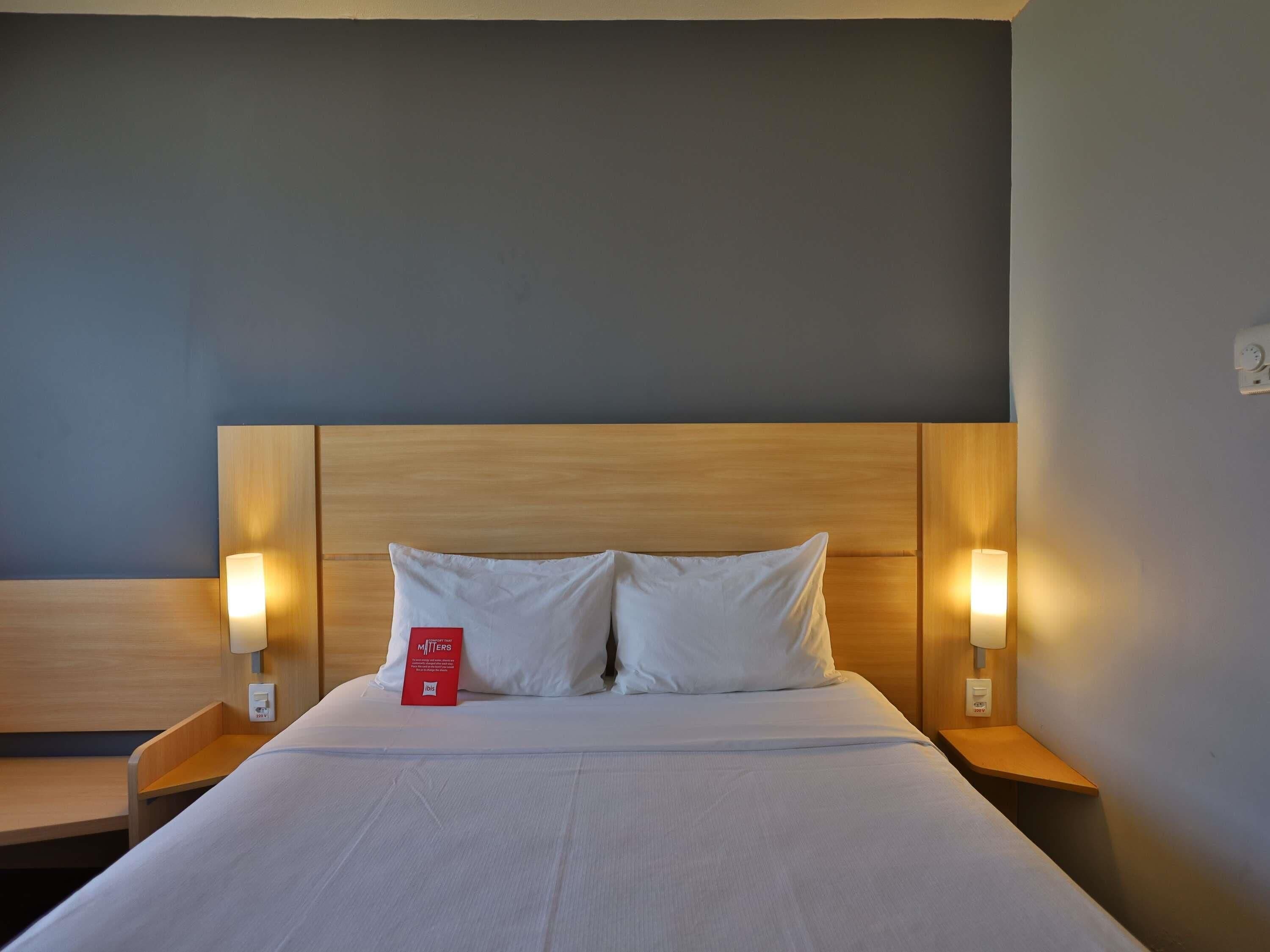 Une chambre d’hôtel avec un grand lit, deux tables de chevet et des lampes fixées au mur.