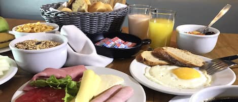 A breakfast table with various food items, including eggs, bread, and a basket of rolls.