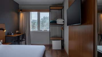 A hotel room with a bed, desk, chair, TV, wardrobe, and a small fridge.