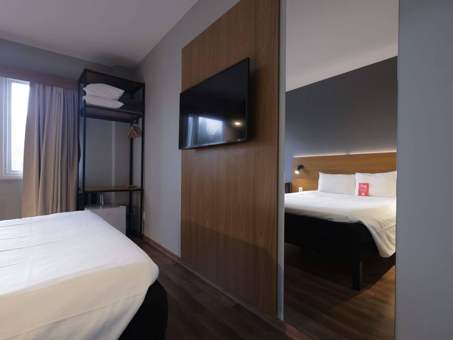 Une chambre d’hôtel équipée d’un lit superposé, d’un lit simple, d’un téléviseur à écran plat fixé sur un panneau en bois et d’une table de chevet avec une lampe.