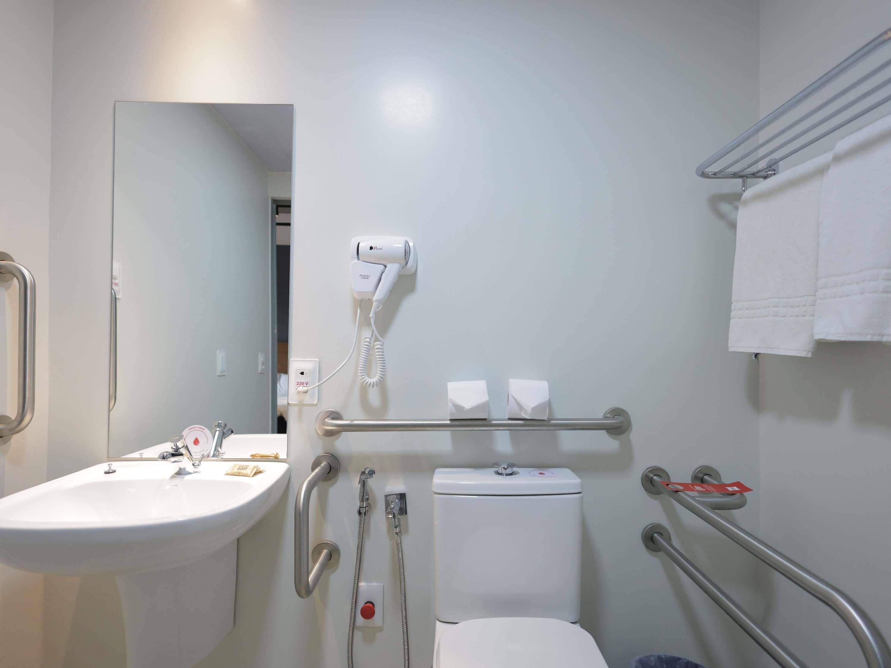 Baño con lavamanos, inodoro, cabezal de ducha manual y secador de pelo fijado en la pared.