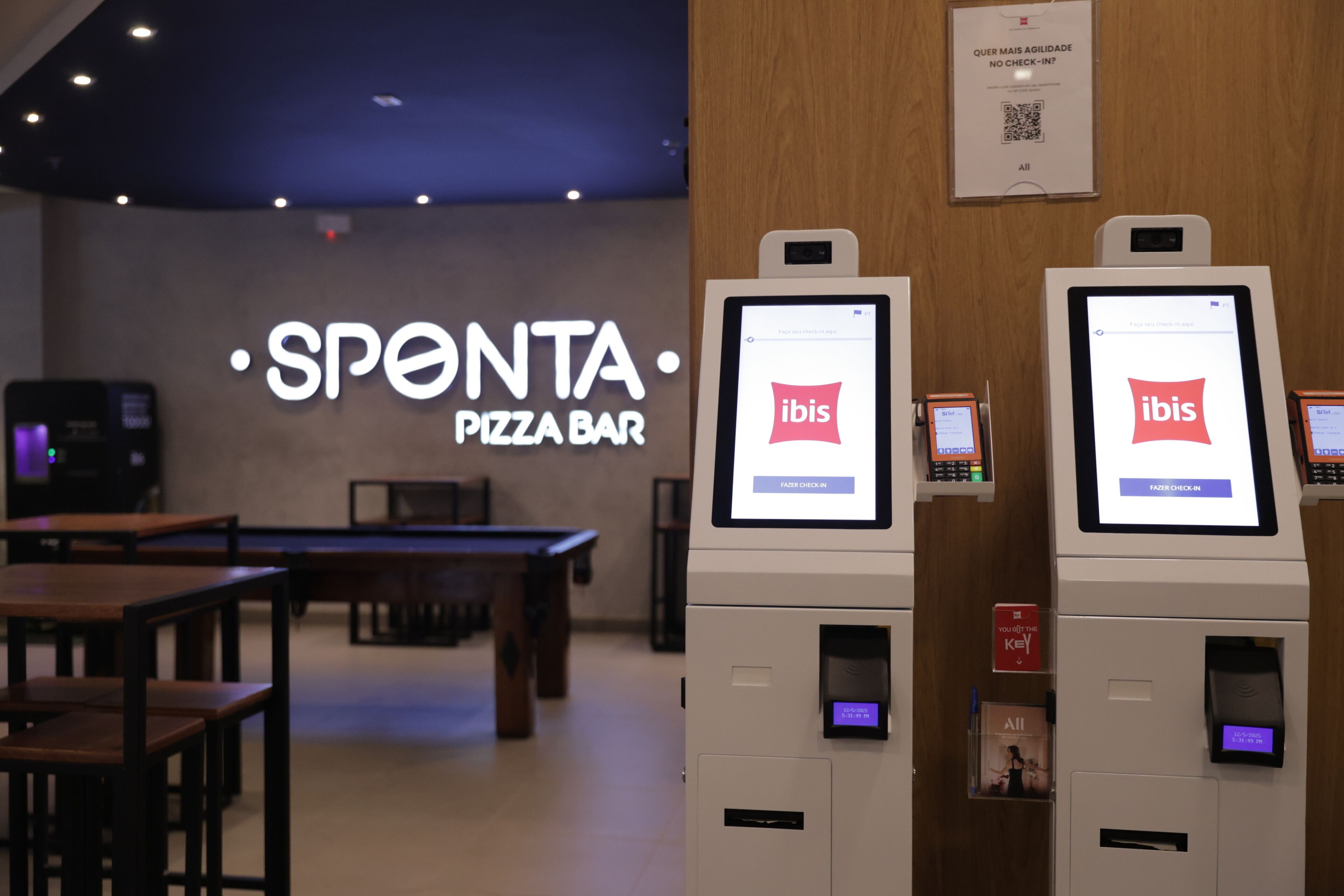 Un bar de pizza con quioscos digitales para el registro, un cartel con código QR y un panel de menú.