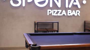 A billiards table with a neon sign for 'SPONTA PIZZA BAR' in the background.