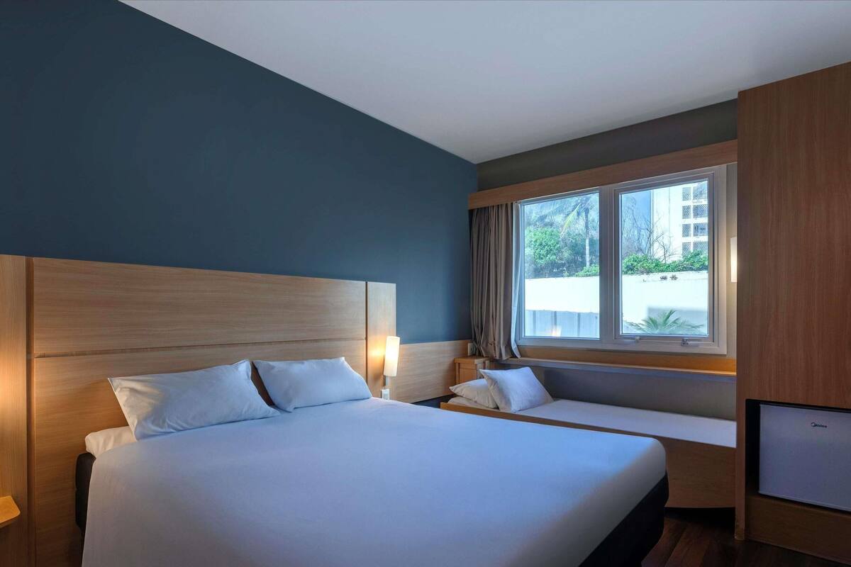 Une chambre d’hôtel avec un grand lit, des tables de chevet, une télévision et une fenêtre avec des rideaux.