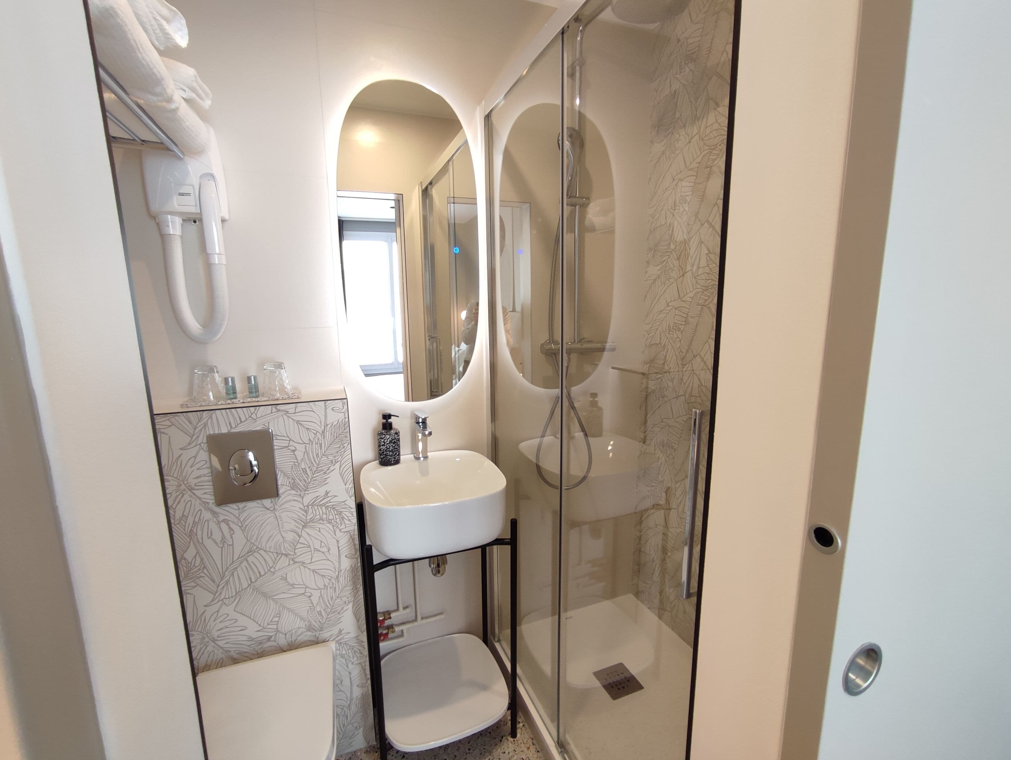 Un baño moderno con cabina de ducha de vidrio, un lavabo blanco y un espejo sobre el lavabo.