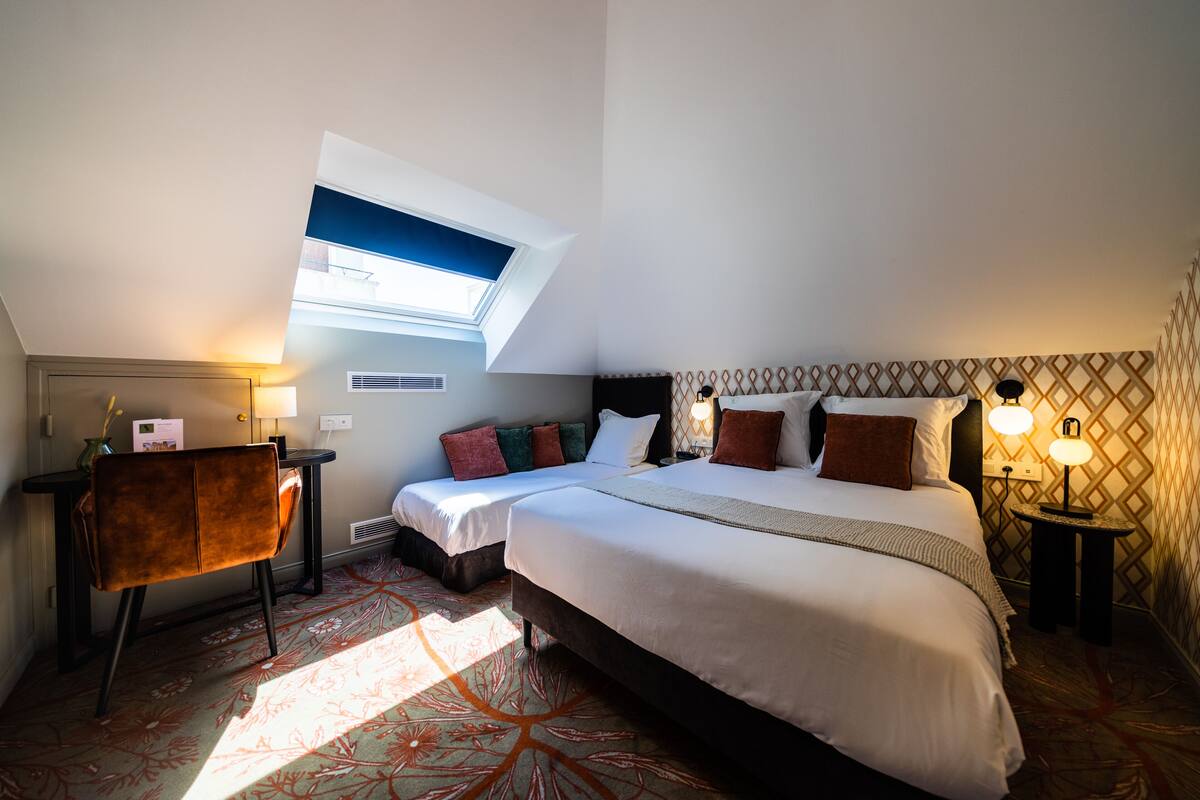 A hotel room with a large bed, two bedside tables with lamps, a desk with a chair, and a window with a view.
