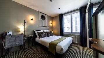Habitación de hotel con una cama bien hecha, un escritorio con silla, una lámpara, una obra de arte en la pared y una ventana con cortinas.