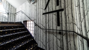 Una escalera con papel tapiz estampado con motivos de árboles, barandilla de metal negro y un ventanal en la parte superior.