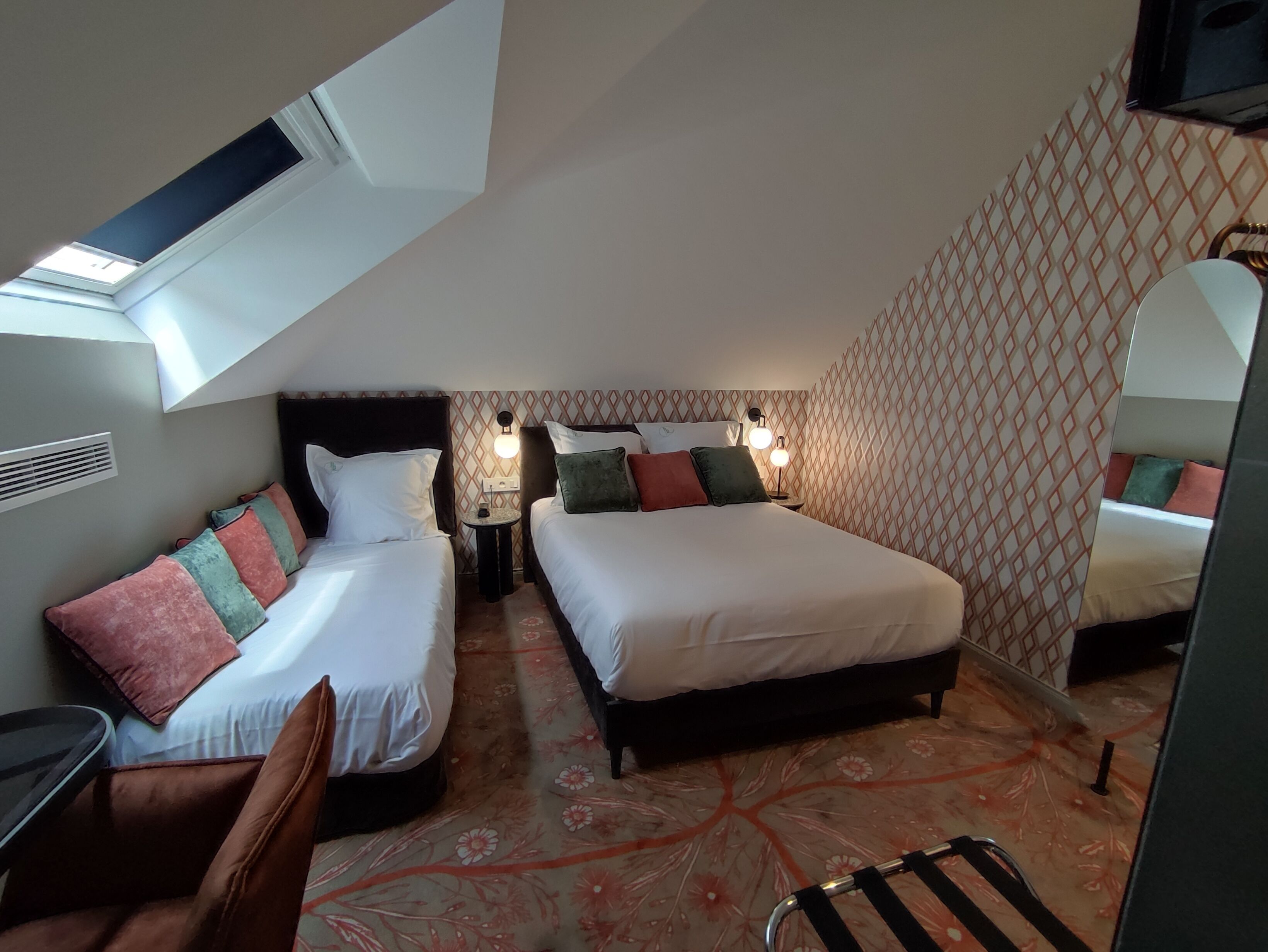 Une chambre d’hôtel avec deux lits, une petite table, une chaise, un miroir et un mur décoré d’un motif.