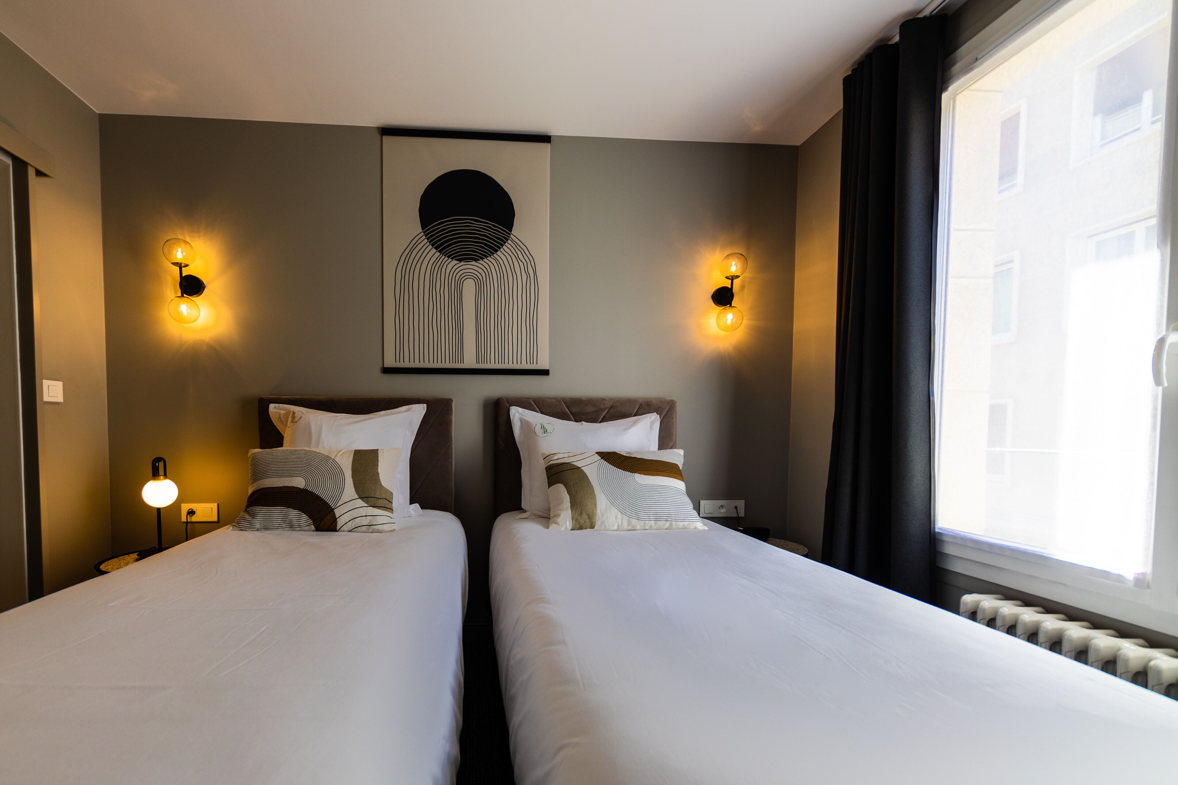 Une chambre d’hôtel avec deux lits, une œuvre d’art accrochée au mur et deux appliques murales.
