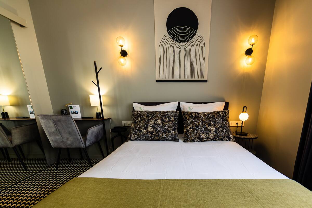 A hotel room with a large bed, two bedside tables with lamps, a desk with a chair, and a wall-mounted artwork.