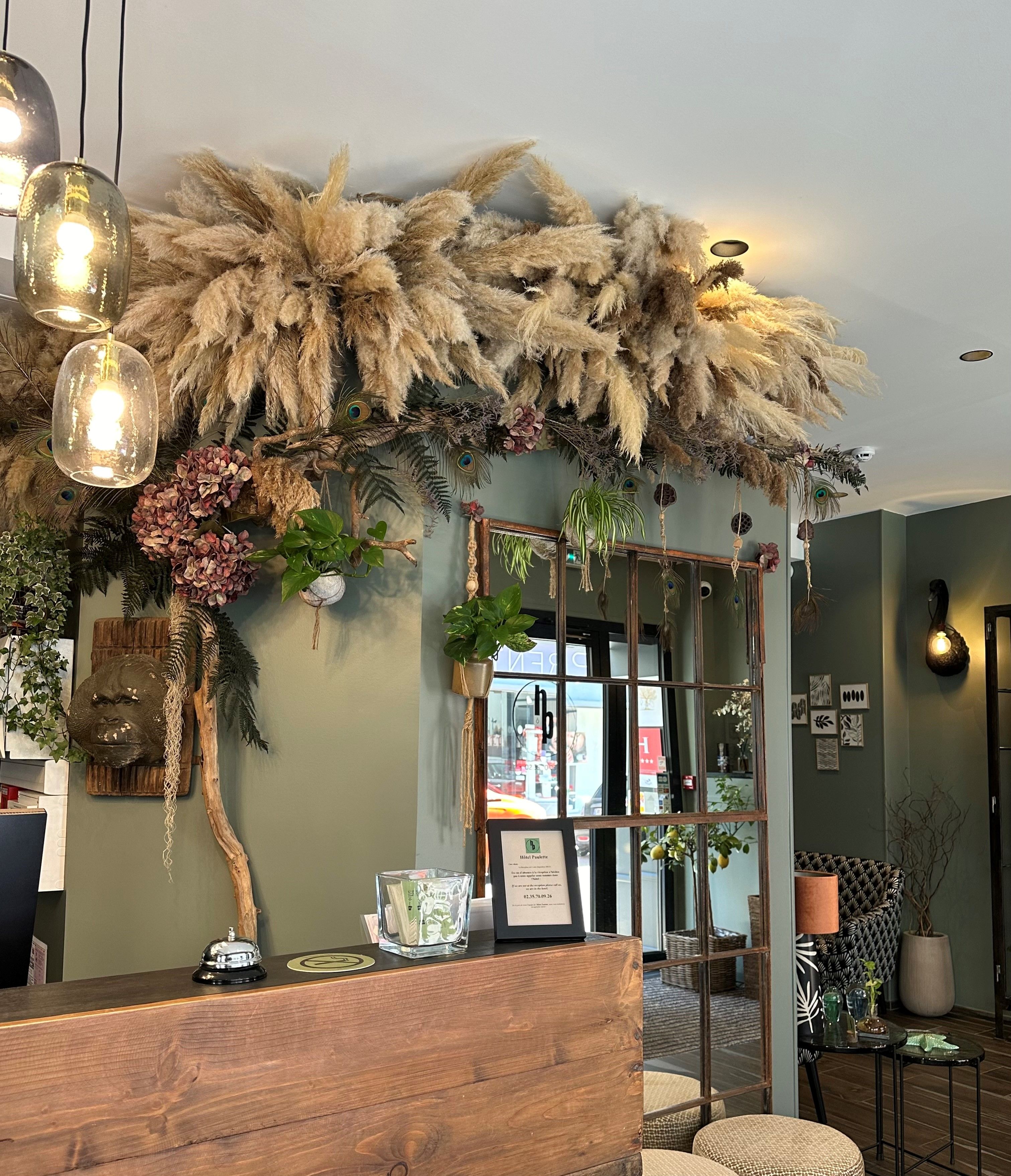 Un espace d’accueil avec un bureau en bois, un panneau d’accueil encadré et une composition florale décorative.