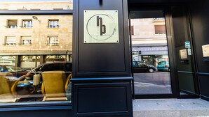 Entrada de un hotel con puerta de cristal, un letrero con el logotipo del hotel y vista de la calle.