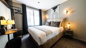 Una habitación de hotel con una cama grande, un escritorio con lámpara, una silla y una mesita con lámpara.