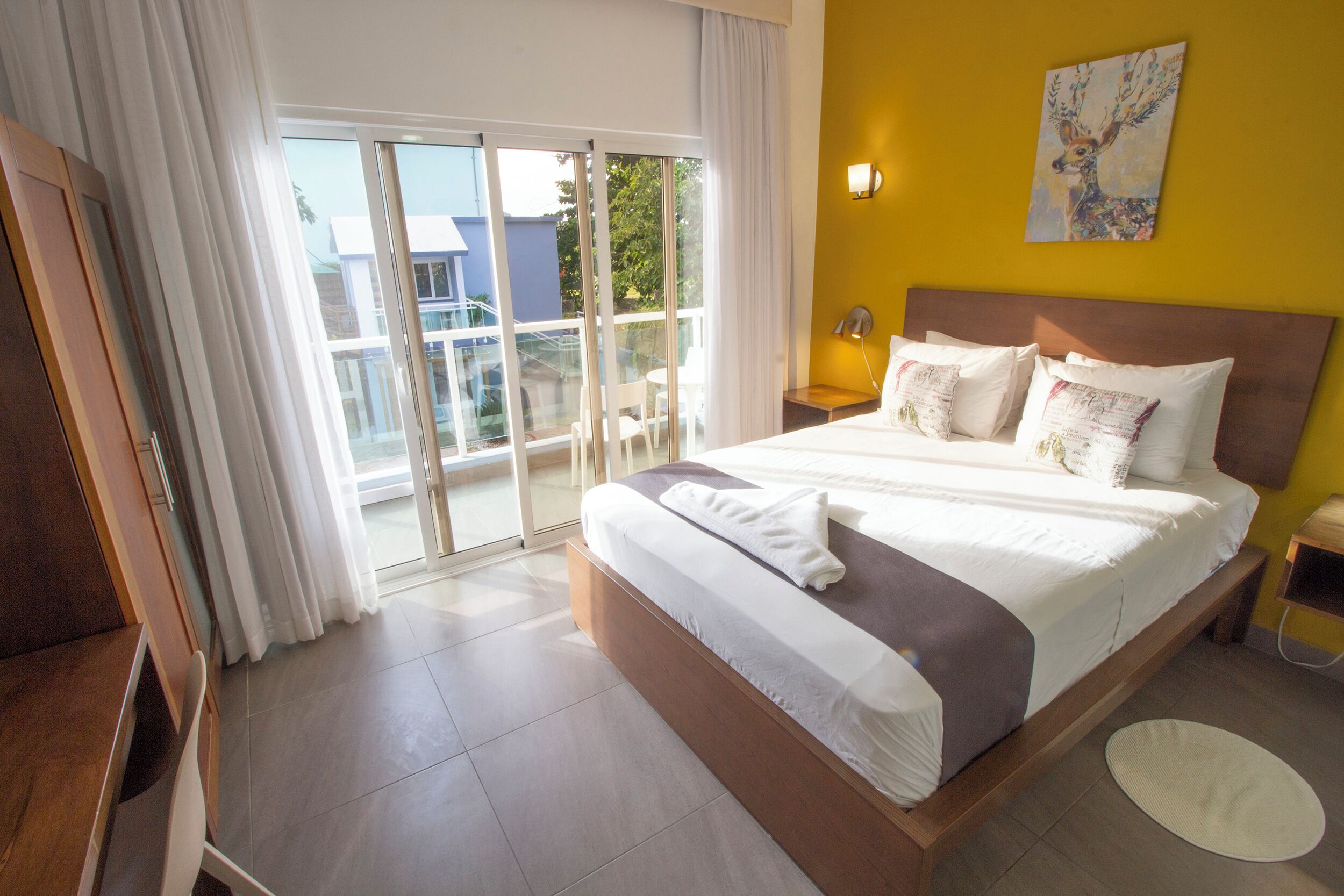 Ein Hotelzimmer mit einem großen Bett, einer Schiebetür zu einem Balkon, einem Nachttisch aus Holz und einer Wandlampe.
