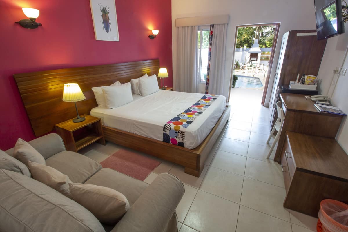 Ein Hotelzimmer mit einem großen Bett, einem Holzkopfstück, einem Schreibtisch mit Telefon und Blick auf den Außenpool.