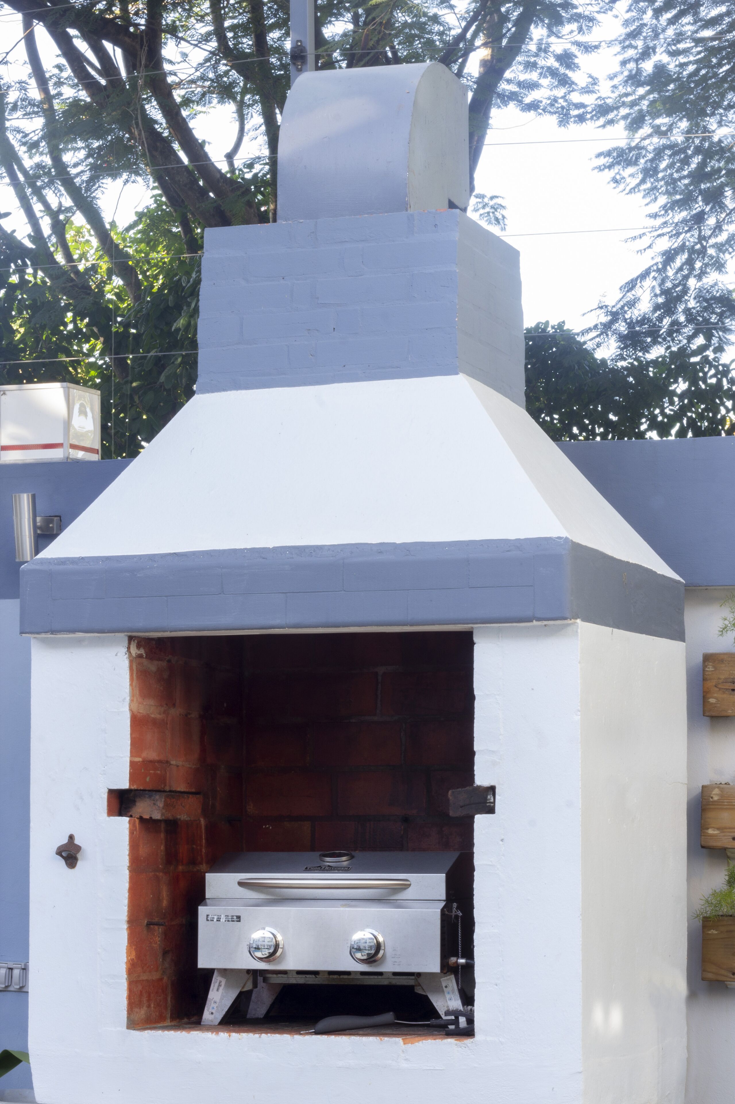 A white outdoor brick oven with a chimney, a metal grill, and a control panel.