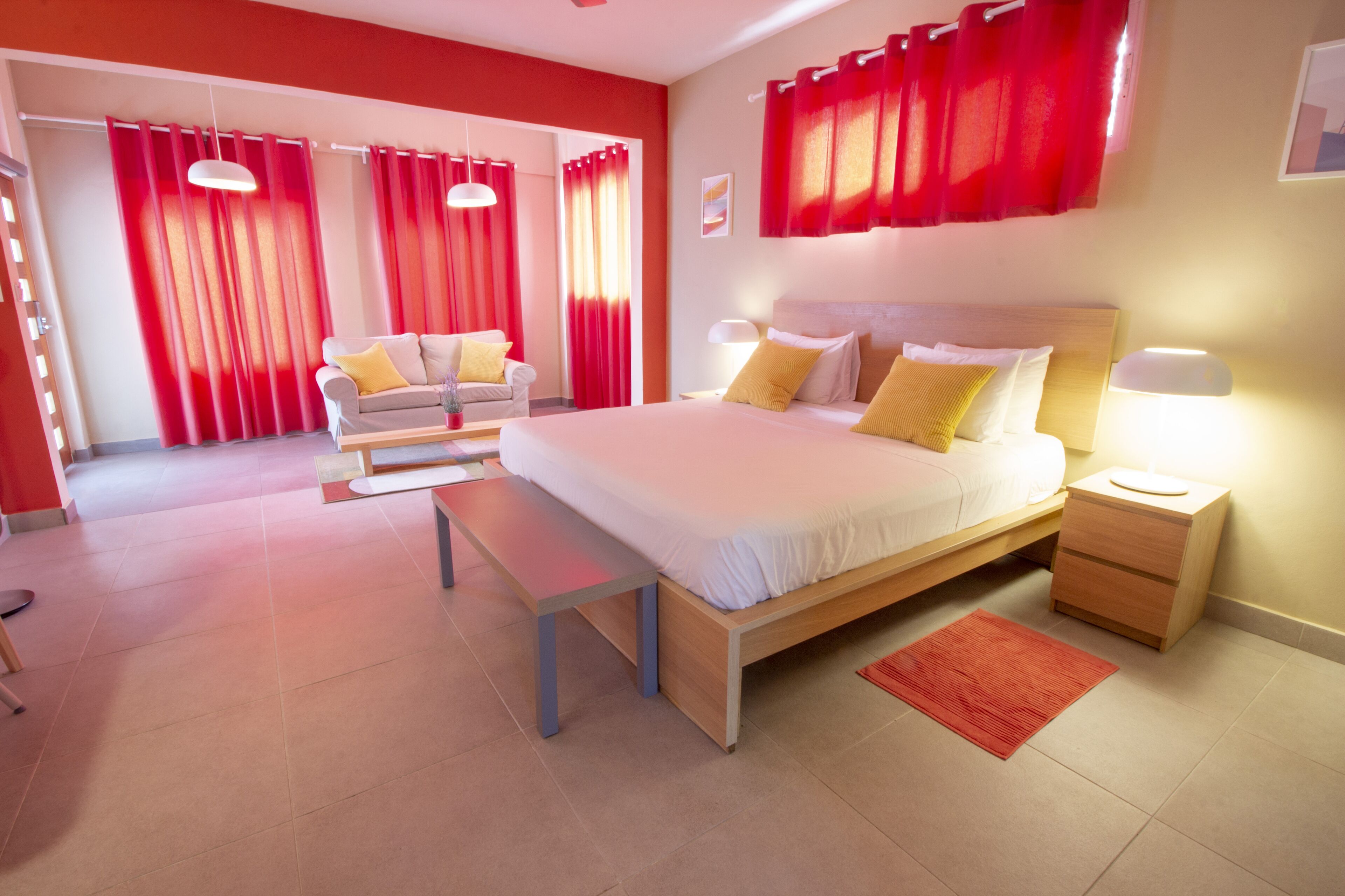 A modern bedroom with a large bed, bedside tables, a bench, and red curtains.