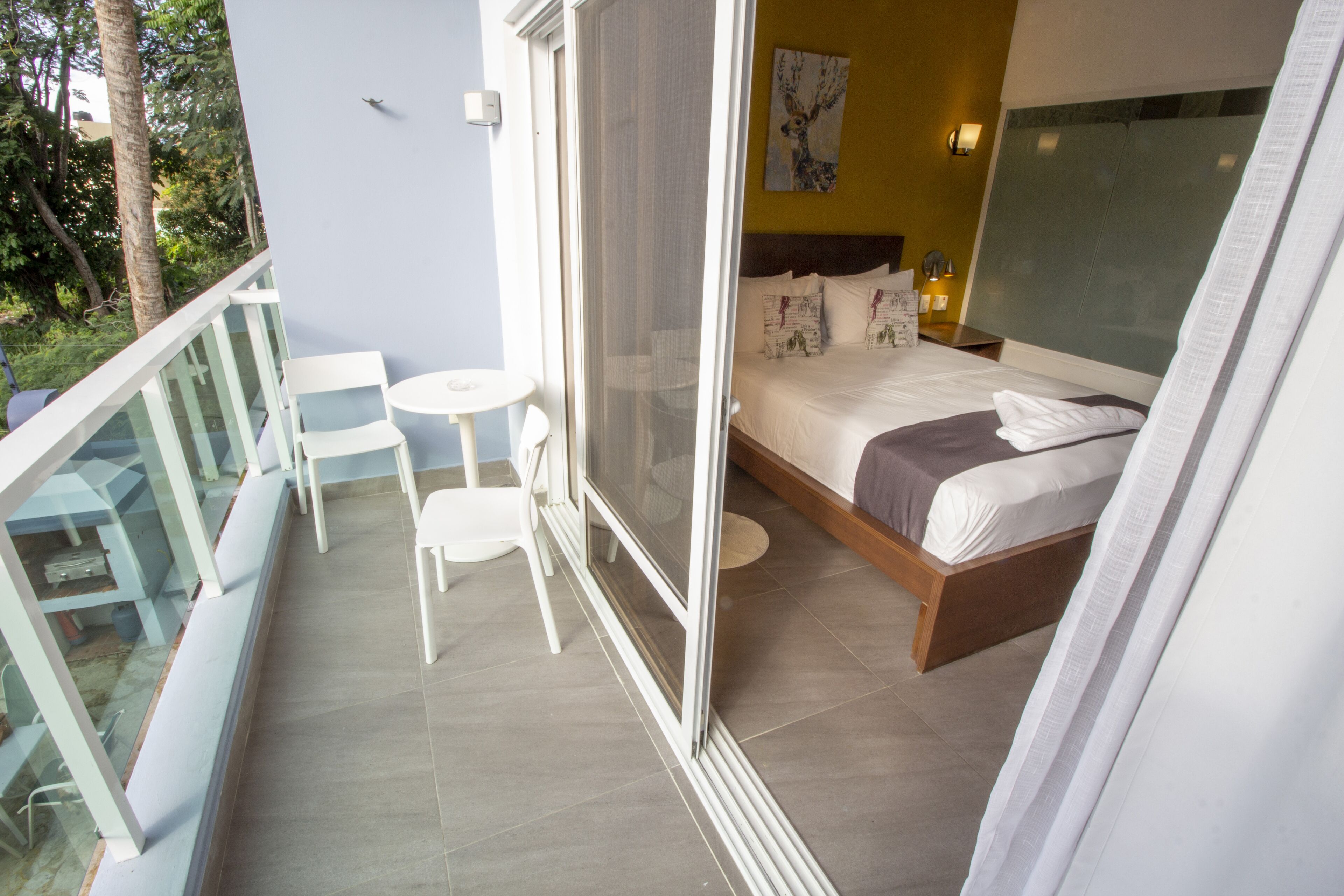 A balcony with a glass railing, a bed with white bedding, and a small white table and chair.