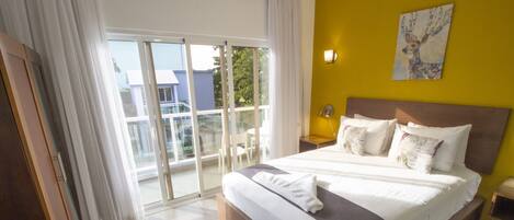 Una habitación de hotel moderna con una cama grande, una puerta corrediza de vidrio al balcón y una pared de acento amarilla.