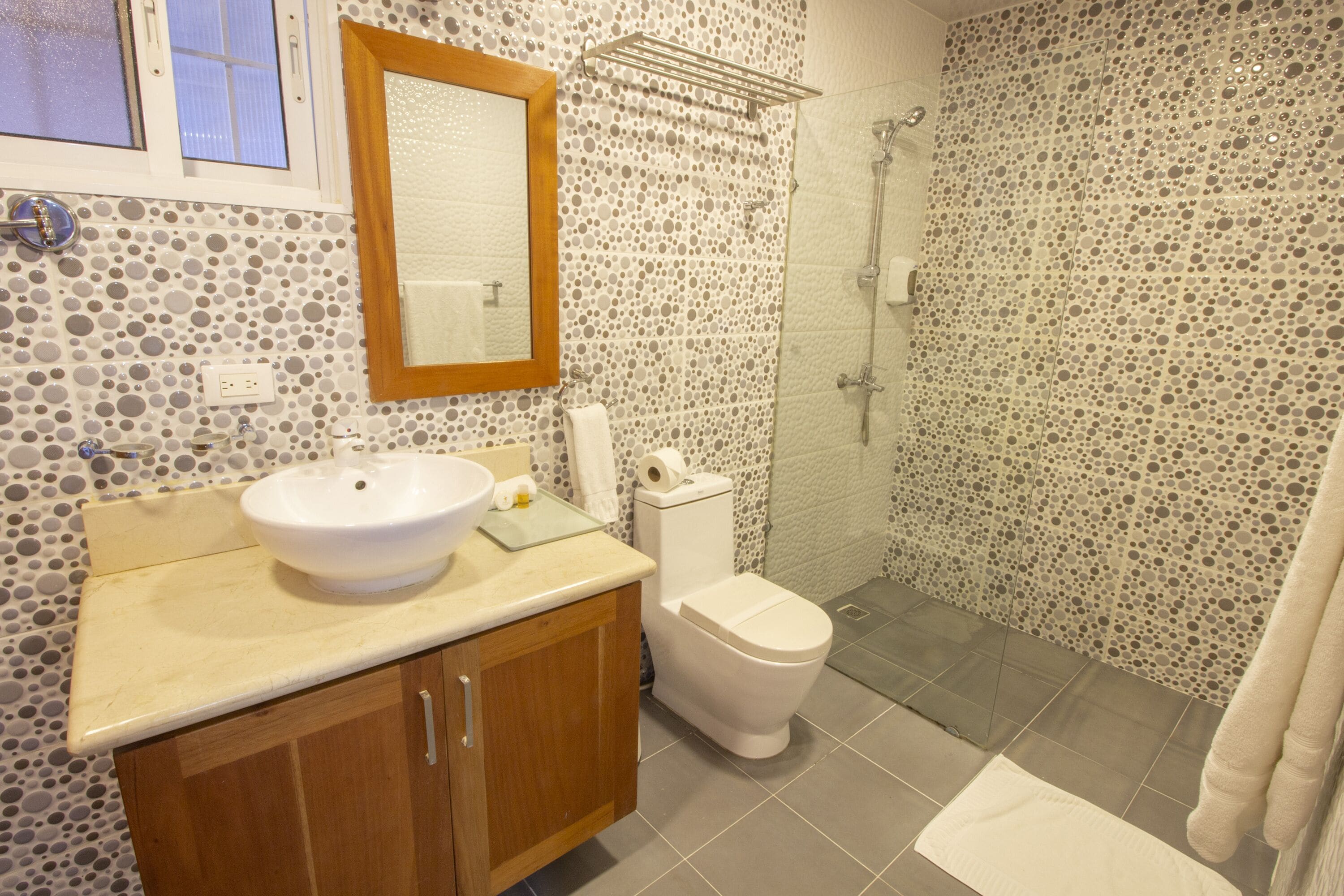 A bathroom with a round sink, wooden cabinets, a toilet, and a shower area.